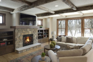Fireplace installation. Stone fireplace with fire burning, in a large living area with exposed beams on ceiling.
